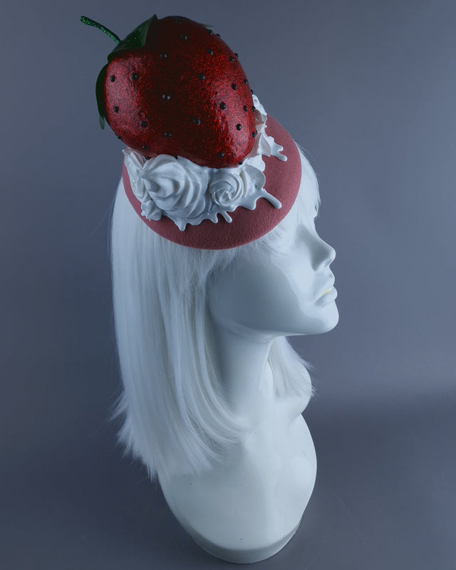 A giant strawberry fascinator hat, set on a pink felt base, dripping with swirls of cream