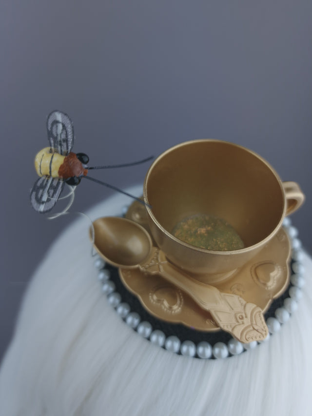 Close up of a gold teacup and bee fascinator, with pearl detailing