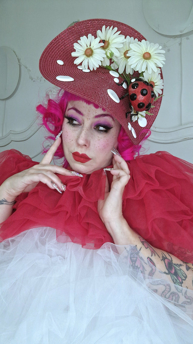 Oversized red mushroom hat decorated with large daises, leaves,and large glitter ladybird