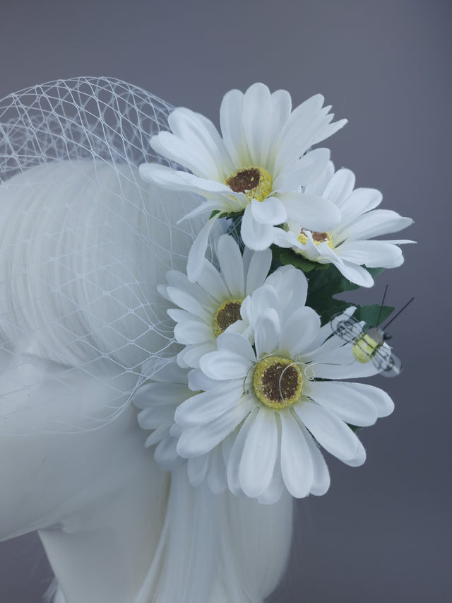 close up of a white headpiece with daisies and bee detailing, and netting veil