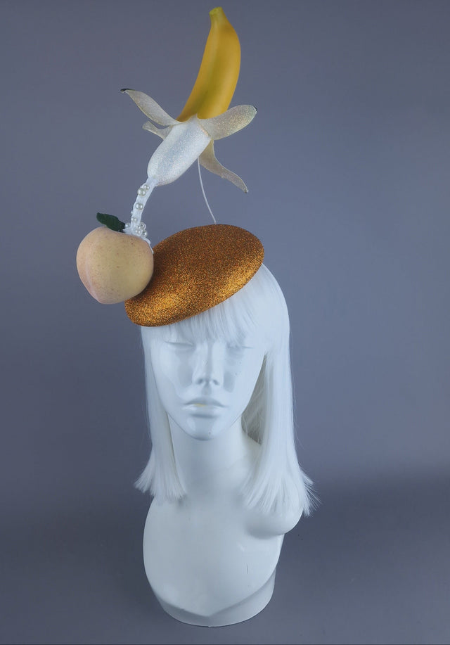 A surreal fascinator hat featuring a glittered banana with a peach and cream detail