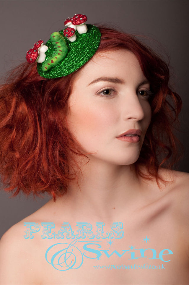 Inspired by Lewis Carrolls "Alice in Wonderland" story, this fascinator base is hand glittered in green with little hand glittered mushrooms sprinkled in clear crystals with a little caterpillar sat on it. The fascinator base is back with leopard print satin and attaches to the hair with a comb and adjustable hat elastic.