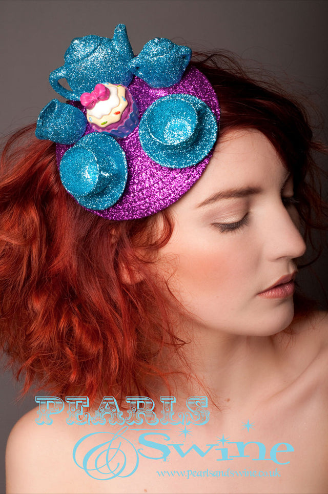 Hand glittered turquoise blue tea set on fuchsia pink glitter fascinator base, complete with a cupcake! These are hand stitched so very secure. The base is backed with leopard print satin and attaches to the hair with a comb and adjustable hat elastic. If you would prefer a different colour combination please contact me. Inspired by Lewis Carroll's "The Mad Hatter's Tea Party".