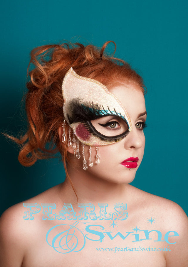 This doll face mask fascinator is covered in iridescent glitter, decorated with blue eyeshadow, pink cheek and 3D eyelashes. The mask is hand blocked, edged in sequins, dripping with fringe beading and backed in leopard print satin. Attaches with a comb and adjustable hat elastic. This super sparkly mask is inspired by my love of dolls.