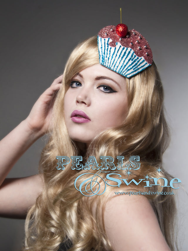 A glittered cupcake cherry fascinator made using hand-blocked millinery felt moulded to fit against your head in a flattering and comfortable way, decorated with hand-stitched silver beads, a red glittered cherry. Backed with satin, this headpiece attaches with a comb and adjustable hat elastic.