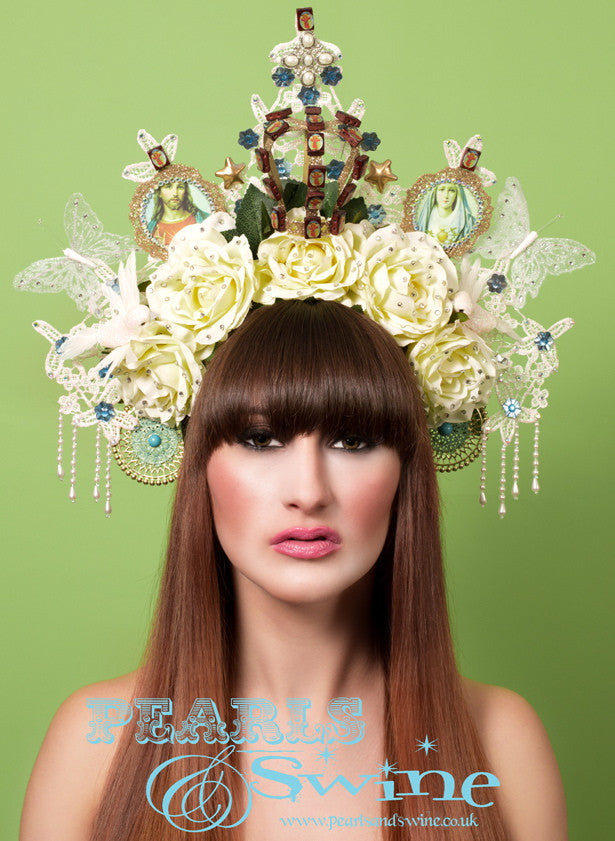 Virgin Mary Headdress "Sacrament" Virgin Mary-inspired headdress which includes an iridescent ivory, glittered lace halo, roses, doves, a gold glittered crown, an image of the Virgin Mary and Jesus, butterflies, stars, Jesus-imprinted wooden beads, crystals, and pearl bead fringes. Set on a headband which is decorated with leaves.