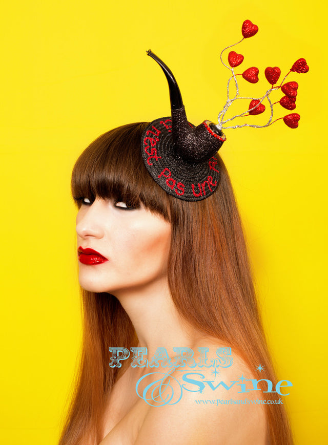 Surreal Pipe Fascinator "Ceci N'est Pas Une Pipe" This surreal pipe fascinator in black glitter, edged with red crystals, silver glittered wire 'smoke' and red glitter hearts set on a fascinator base with "Ceci N'est Pas Une Pipe" in red glitter. Attaches with a comb and hat elastic. This quirky headpiece is part of a collection of pipe headpieces. Inspired by "Ceci n'est pas une pipe" by René Magritte, a Belgian surrealist artist aka "This is not a pipe". Nope, it's a fascinator... Perfect for fans of