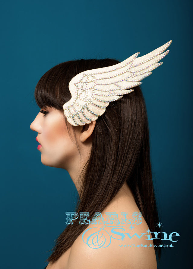 Iridescent glitter wing fascinator edged with feather detailing done in rainbow crystals. Hand blocked and backed with ivory satin, attaches to the hair with a comb and adjustable hat elastic. A perfect bridal headpiece, inspired by Icarus who flew too close to the sun.