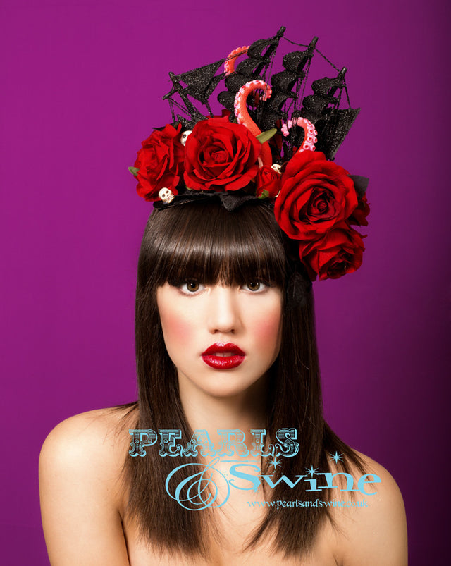 Black glittered ship on a sea of red roses and black leaves, being attacked by a giant octopus's tentacles, sprinkled in a few skulls. This is a piece of wearable art! Set on a wired curved sinamay base backed with leopard print satin. Attaches with a comb and hat elastic. Bobby pins will secure this creation further if required. This pirate ship headpiece is fabulously gothic and perfect for Royal Ascot or any races.