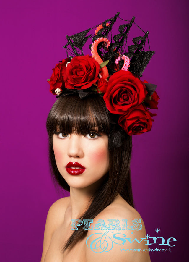 Black glittered ship on a sea of red roses and black leaves, being attacked by a giant octopus's tentacles, sprinkled in a few skulls. This is a piece of wearable art! Set on a wired curved sinamay base backed with leopard print satin. Attaches with a comb and hat elastic. Bobby pins will secure this creation further if required. This pirate ship headpiece is fabulously gothic and perfect for Royal Ascot or any races.