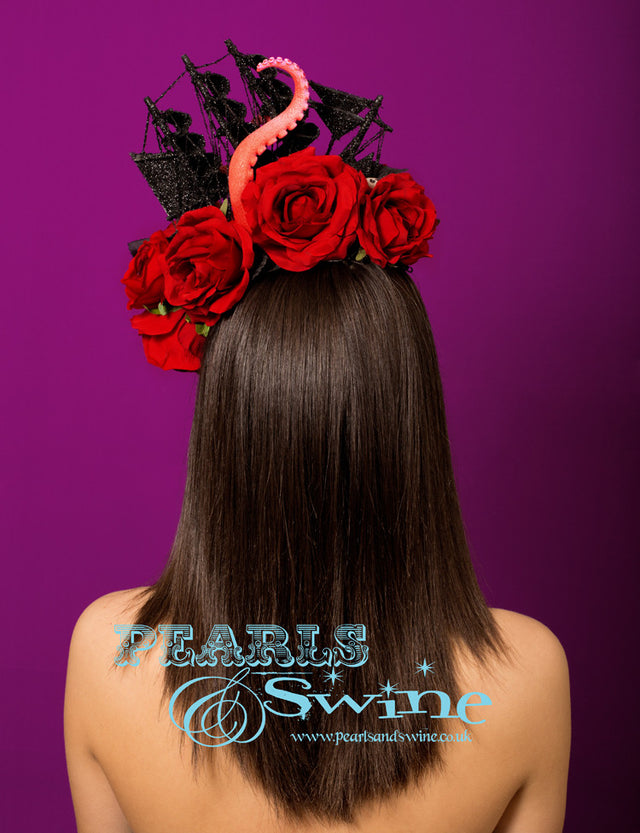 Black glittered ship on a sea of red roses and black leaves, being attacked by a giant octopus's tentacles, sprinkled in a few skulls. This is a piece of wearable art! Set on a wired curved sinamay base backed with leopard print satin. Attaches with a comb and hat elastic. Bobby pins will secure this creation further if required. This pirate ship headpiece is fabulously gothic and perfect for Royal Ascot or any races.