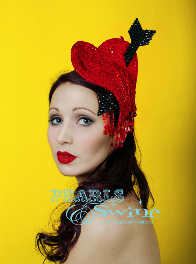 Hand blocked red glitter heart, embellished with red lace and beads. Pierced with a black gem arrow, dripping with red fringe beading. Set on a red lace headband. This is a one of a kind headpiece. Perfect for Valentines Day, a wedding or Ascot.
