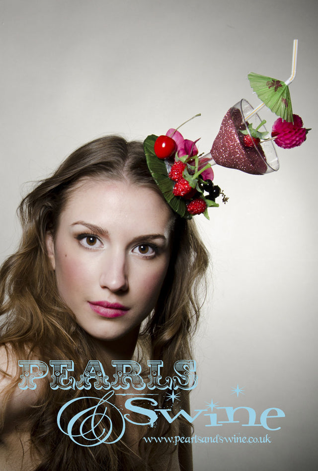 Pink glitter cocktail fascinator decorated with berries, cherries fruit, bougainvillea flowers and an umbrella. The fascinator base covered is leaves and is backed with leopard print satin. Attaches with a comb and adjustable hat elastic. This lightweight quirky headpiece is perfect for Royal Ascot or a cocktail lover.