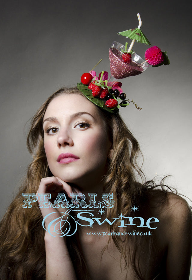 Pink glitter cocktail fascinator decorated with berries, cherries fruit, bougainvillea flowers and an umbrella. The fascinator base covered is leaves and is backed with leopard print satin. Attaches with a comb and adjustable hat elastic. This lightweight quirky headpiece is perfect for Royal Ascot or a cocktail lover.