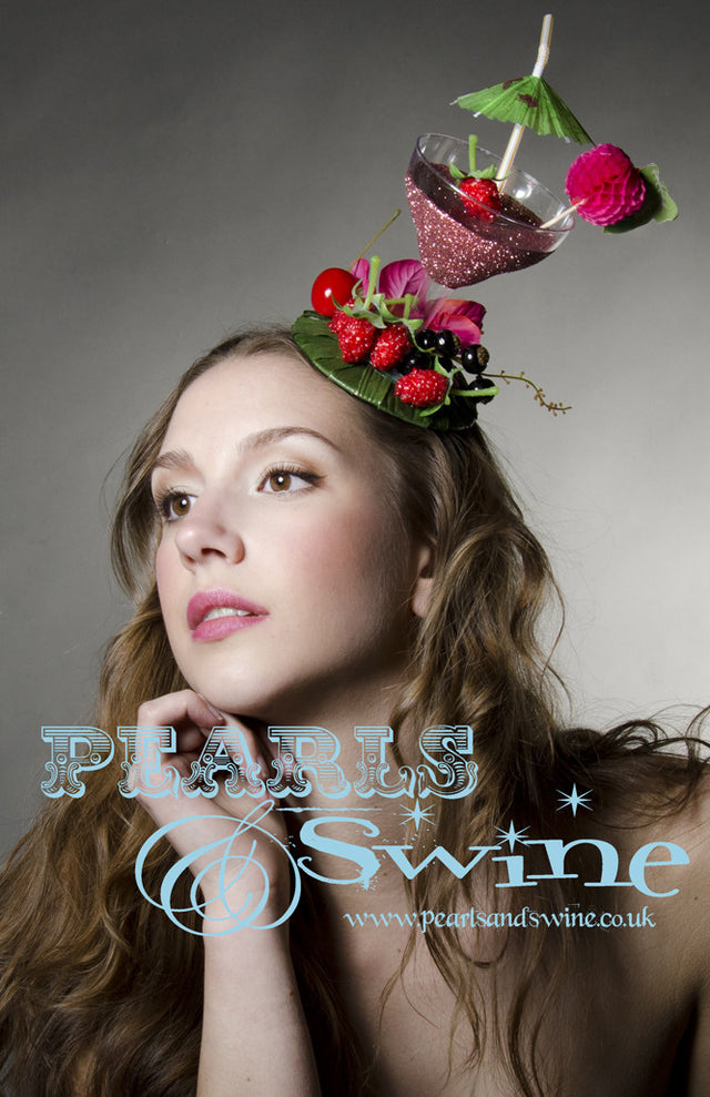 Pink glitter cocktail fascinator decorated with berries, cherries fruit, bougainvillea flowers and an umbrella. The fascinator base covered is leaves and is backed with leopard print satin. Attaches with a comb and adjustable hat elastic. This lightweight quirky headpiece is perfect for Royal Ascot or a cocktail lover.