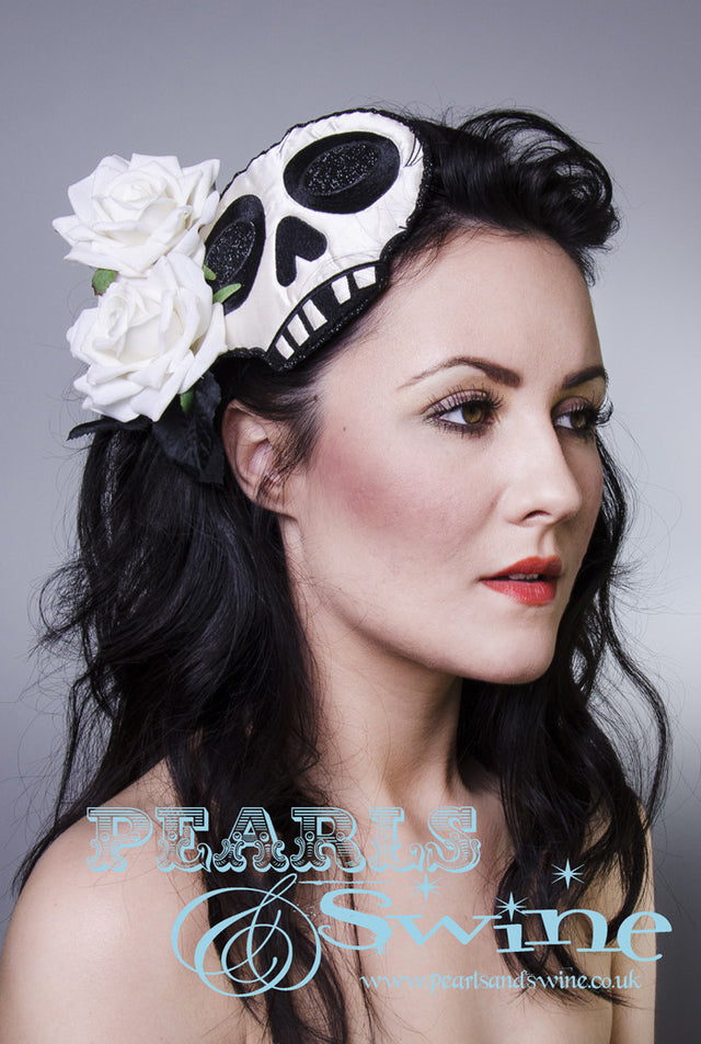 Ivory skull fascinator, edged and decorated with black glitter and ivory velvet roses. Set on a black straw base, attaches with a comb and adjustable hat elastic. Perfect for day of the dead, goth and Halloween fashion lovers!