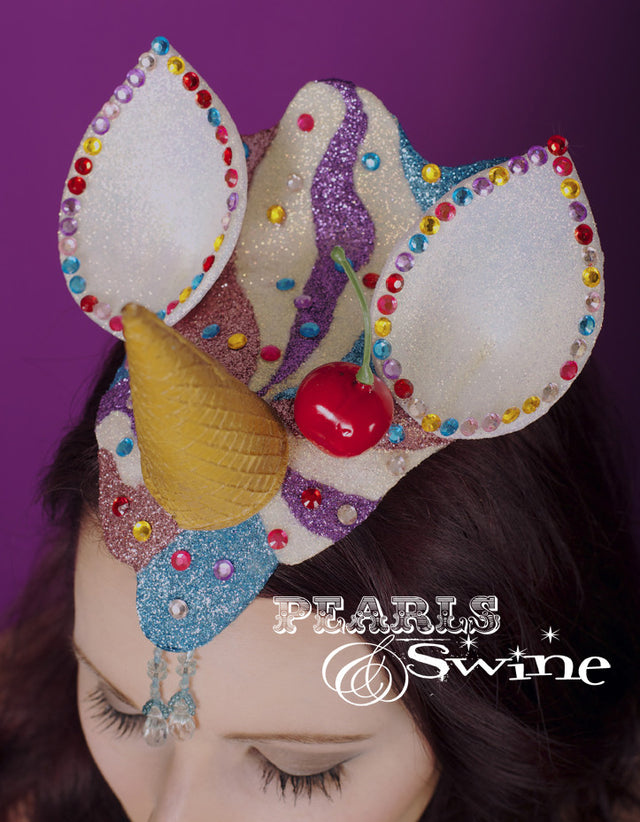 Unicorn Ice Cream fascinator "Sprinkles" This dropped ice cream cone that doubles as a unicorn horn is hand-moulded and glittered in pink, blue, and iridescent white. The ears are decorated with gem"100's & 1000's", and the ice cream cone unicorn horn has a cherry on top. Backed with leopard print satin it attaches with a comb and hat elastic.