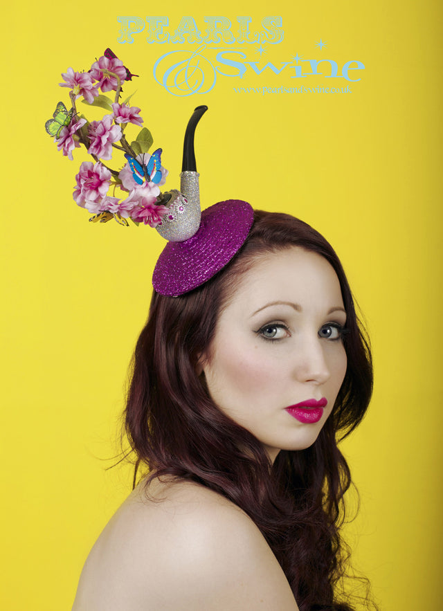 Butterfly and pipe fascinator, featuring cherry-blossom and butterfly 'smoke' emerging from a sparkly pipe. Set on a fuchsia-pink glitter base, the butterfly and pipe fascinator is backed with satin and attaches with a comb and adjustable hat elastic. "Opium" Butterfly & Pipe fascinator is part of my "This is not a Pipe" millinery collection inspired by René Magritte. With an 11cm base this is perfect for Royal Ascot, a wedding or lovers of René Magritte's art.