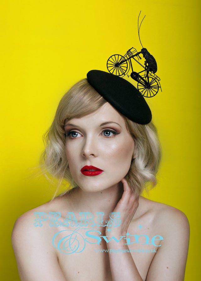 Charmingly quirky yet elegant black blocked felt hat decorated with an old-fashioned miniature bicycle in metal and a black glitter bug perched on the seat. The insect has wire arms and legs so can be gently removed and reattached. This hat has a satin lining and attaches with a comb and adjustable hat elastic. People went totally crazy when I showed this hat on my social media so I am certain this hat is one that will charm everyone who sees it, it's surreal, funny, cute but slightly French somehow.