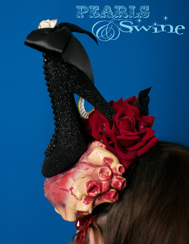 Anatomical heart hat, being crushed by a black glittered high heel shoe, decorated with a skull bow and black gems. This one of a kind, anatomical heart hat also has red velvet roses, a snake, and drips with red fringe beading. Attaches with a comb and adjustable hat elastic. This Halloween style hat is perfect for heart-breakers and devil-women. It's a piece of wearable art, a wicked take on Schiaparelli's shoe hat. The sort of Halloween hat you want to keep on display in a glass cabinet all year round.