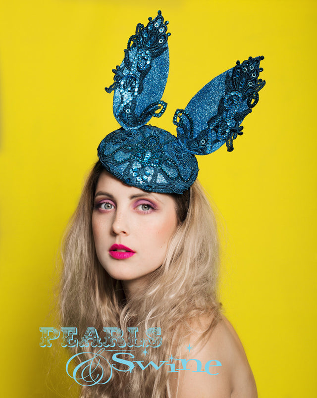 Turquoise blue glitter bunny-ears on a blocked felt hat is embellished with lace and crystals. Attaches with a comb and hat elastic. This bunny hat is totally opulent and eye catching, it's very sparkly. Bunny rabbit ear headpieces are very common but this headpiece is something a bit special and unique. Totally perfect for Royal Ascot or a wedding or party!