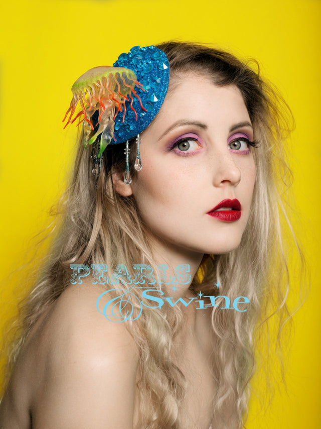 Unique jellyfish fascinator set on a sea of turquoise blue jewelled bubbles (gems) and glitter, dripping with blue fringe beading to add movement to the fascinator. The 11cm round fascinator base is backed in satin leopard print and it attaches with a comb and adjustable hat elastic. You could wear this jellyfish fascinator anywhere, as it's not too big, perfect for mermaids and sea lovers.