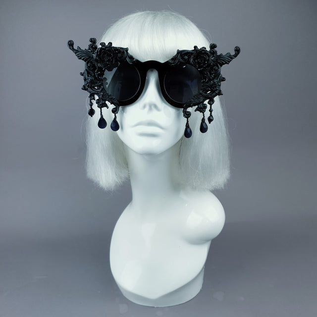 Black filigree ornate sunglasses with hand moulded filigree, cherubs, and roses decorations, and black jewels. Displayed on a mannequin head.