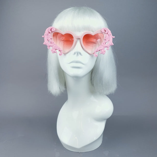 A pair of pink filigree heart-shaped sunglasses displayed on a mannequin head.