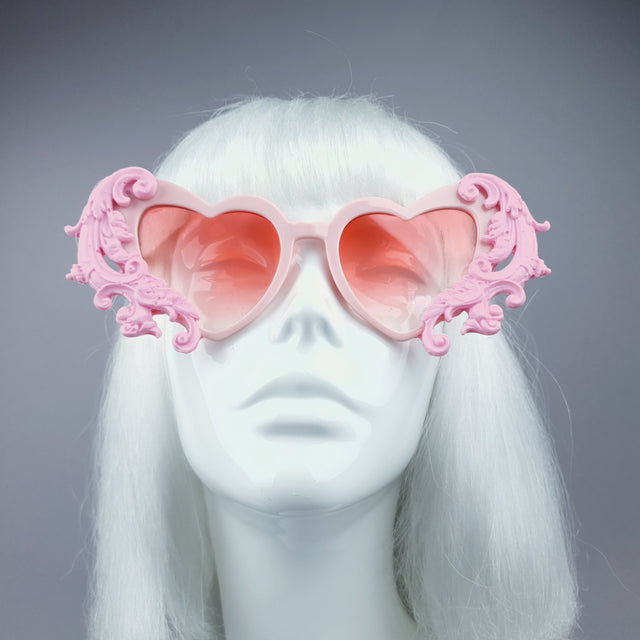 A pair of pink filigree heart-shaped sunglasses displayed on a mannequin head.