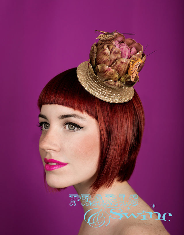 A quirky, cute artichoke set on a light-gold glitter fascinator base decorated with grasshoppers feasting on the artichoke. It is backed with leopard-print satin and attaches with a comb and adjustable hat elastic. This limited edition whimsical hat is ideal for vegetarians and insect lovers.