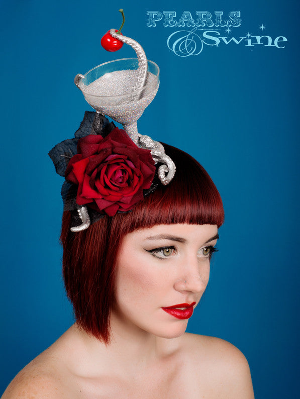 Surreal diamond glitter cocktail with a tentacle, pinching the cherry. Decorated with more silver tentacles, red velvet rose and black leaves. This is set on a black glittered fascinator base which is backed with leopard print satin and attaches with a comb and adjustable hat elastic. This is a piece of wearable art, i recommend you display it in a cabinet when not wearing it.