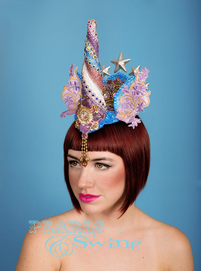 One of a kind detailed unicorn headdress, complete with a bejewelled unicorn horn, ears with lace detailing and silver stars. And a central jewel detail that drips from the front. This unicorn headdress is hand blocked, backed with leopard print satin, and attaches with a comb and adjustable hat elastic. Ideal surreal headpiece of wearable art for lovers of ponies and unicorns. Disclaimer: No unicorns were harmed in the making of this piece!