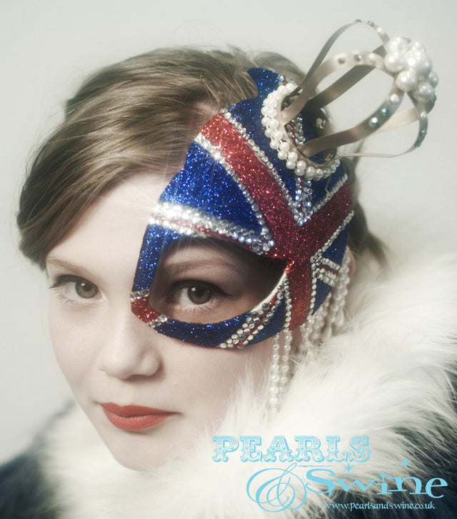 Union Jack Half Mask Fascinator "Regency" This half mask fascinator has a glittered Union Jack with a gold crown decorated in pearls, crystals, and pearl beading. Attaches with a comb.
