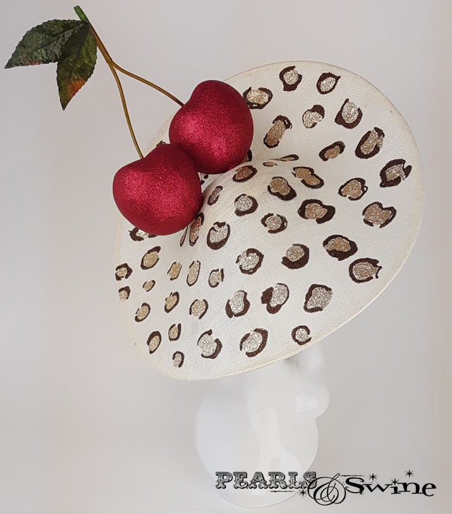 Giant red glittered cherries on a large ivory sinamay hat base, hand painted with glittered leopard print