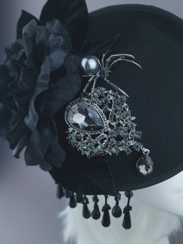 Close up shot of a black felt hatintaor with black roses, fringe beading & velvet leaves. Decorated with a spider and a large sparkling jewel.