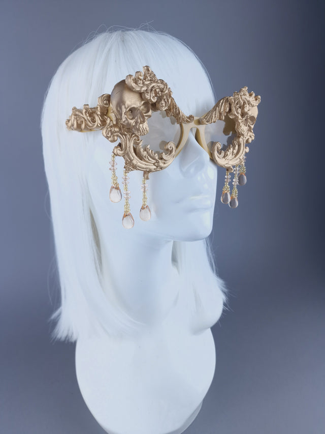 Decorate arm of a pair of ornate gold cat-eye sunglasses with filigree, skull, and beading details displayed on a mannequin head.