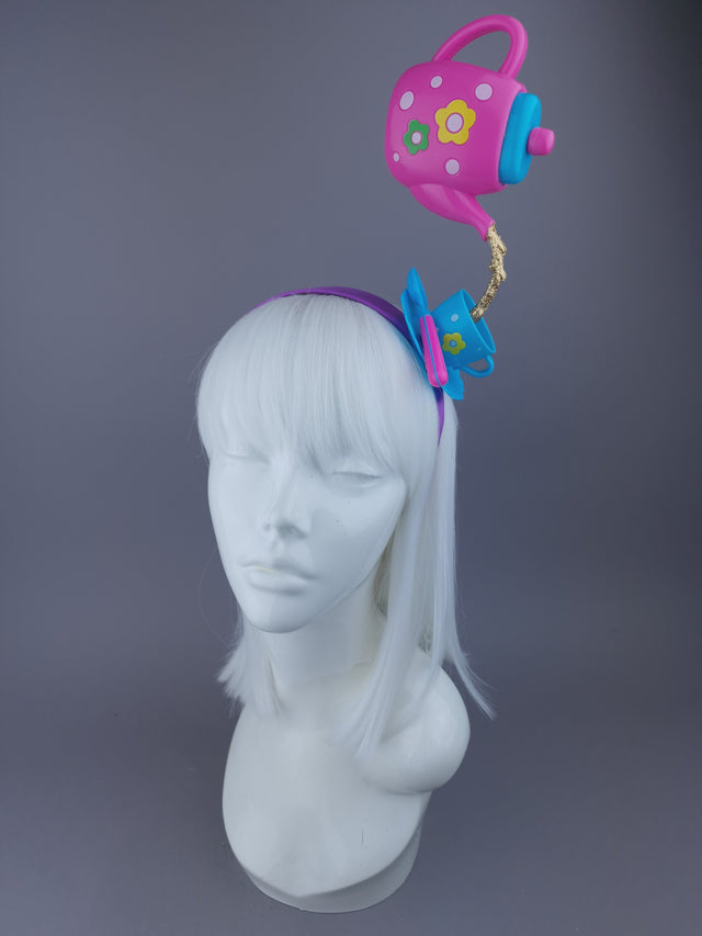 Pink teapot pouring tea into a tea cup set on a purple alice band