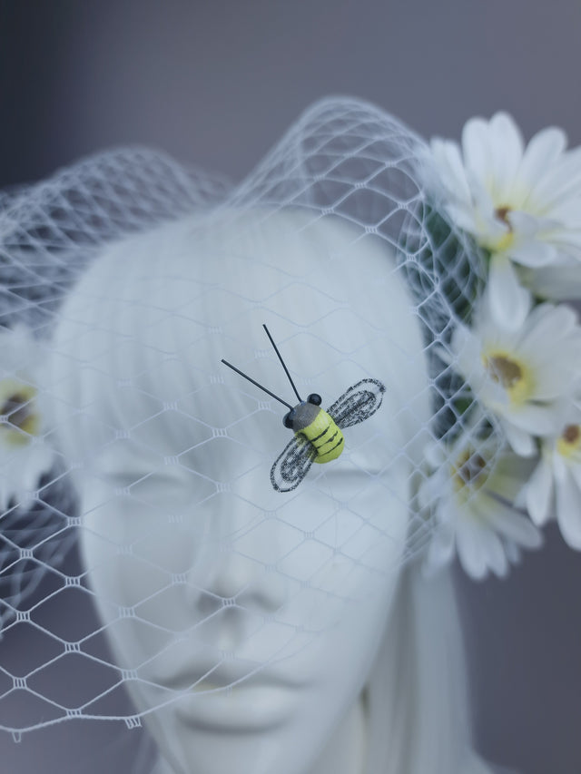 Close up shot of bee on white headpiece with daisies and bee detailing, and netting veil