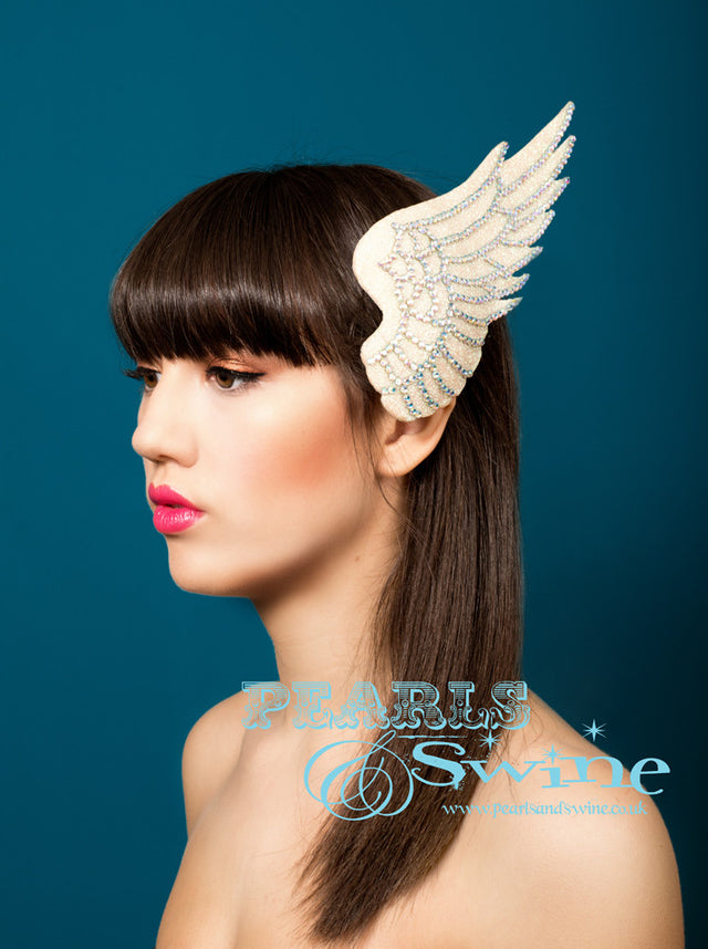 Iridescent glitter wing fascinator edged with feather detailing done in rainbow crystals. Hand blocked and backed with ivory satin, attaches to the hair with a comb and adjustable hat elastic. A perfect bridal headpiece, inspired by Icarus who flew too close to the sun.