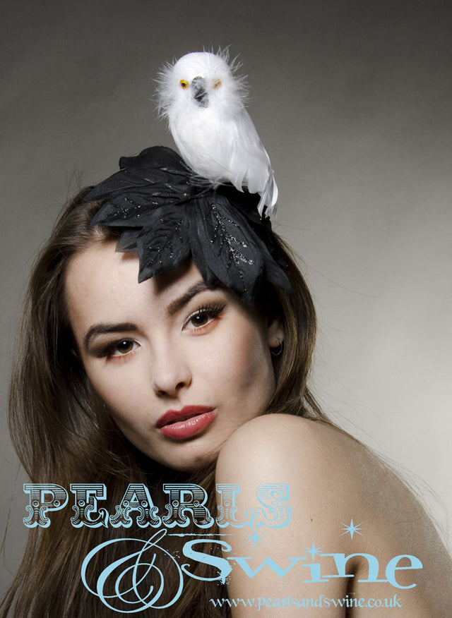 White owl perched on a fascinator base covered with black, hand-glittered leaves. Attaches with a comb and adjustable hat elastic. Limited Edition.