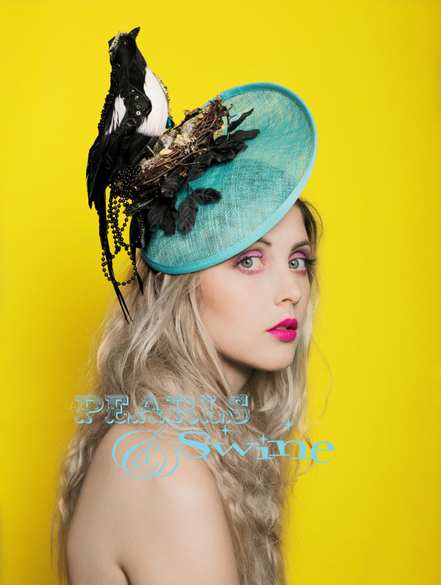 Very detailed, one of a kind artificial magpie in it's nest set on an aqua blue hat. The magpie is decorated with lace, sequin and jewels, perched in a nest strewn with jewels and treasures. This is set on a headband, if needed bobby pins will help to secure firmly to the head.  This hat is perfect for ladies day at Royal Ascot or a wedding.