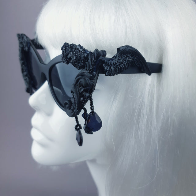 Close-up of the decorated arm of a pair of ornate black filigree cat eye sunglasses. A wing with dripping beading.
