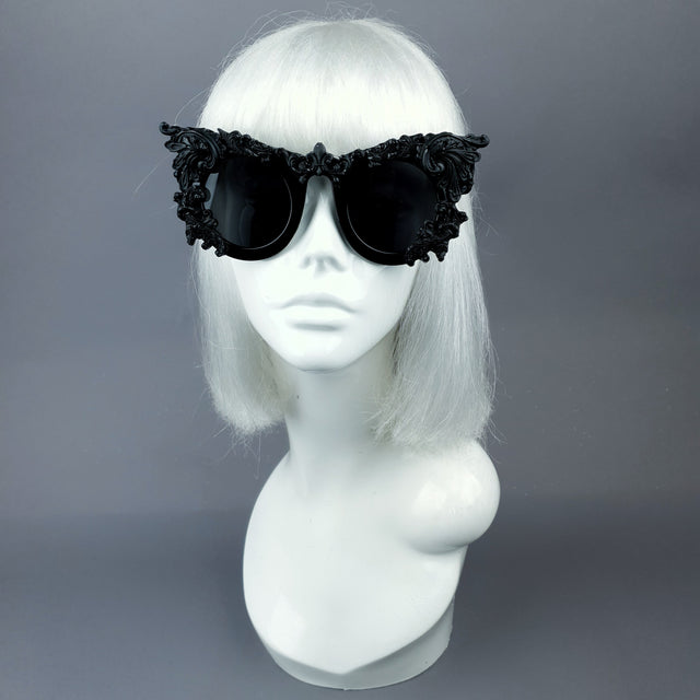 A pair of ornate sunglasses with black filigree design displayed on a mannequin head.