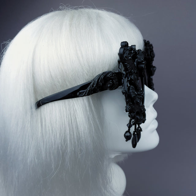 Arm detail of black filigree ornate sunglasses with hand-moulded filigree, cherubs, and roses decorations, and black jewels. Displayed on a mannequin head.