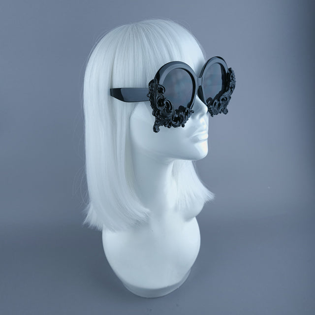 Side view of oversized black round sunglasses decorated with filigree, displayed on a mannequin head