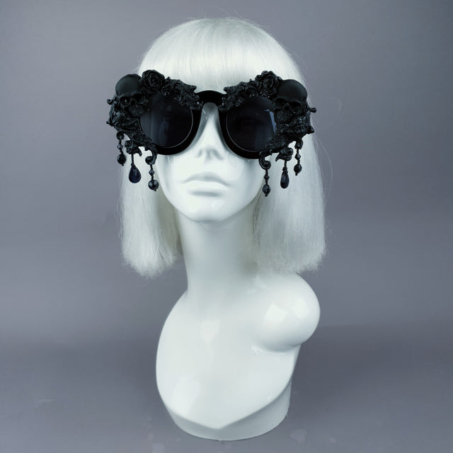 A pair of oversized, ornate black sunglasses with skull, filigree, and bead details displayed on a mannequin head.