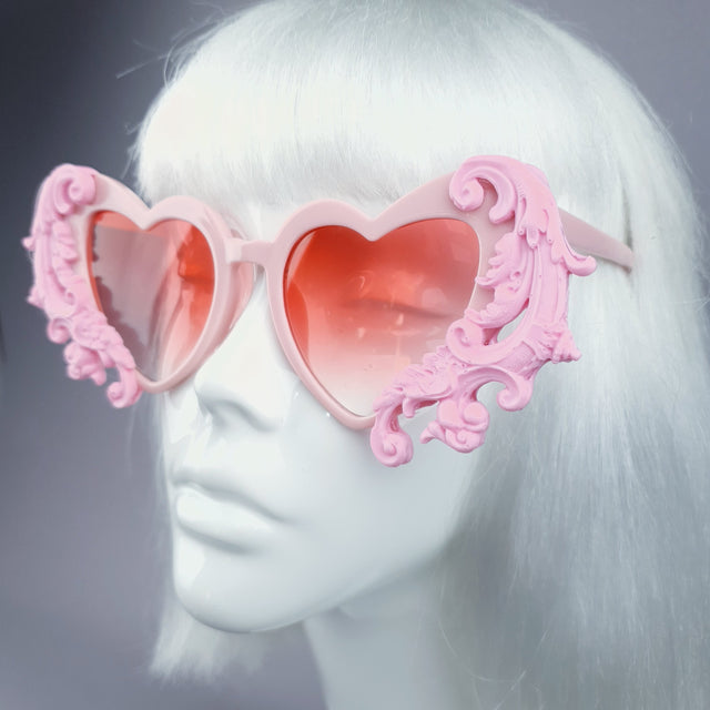 Close-up of a pair of pink filigree heart-shaped sunglasses displayed on a mannequin head.