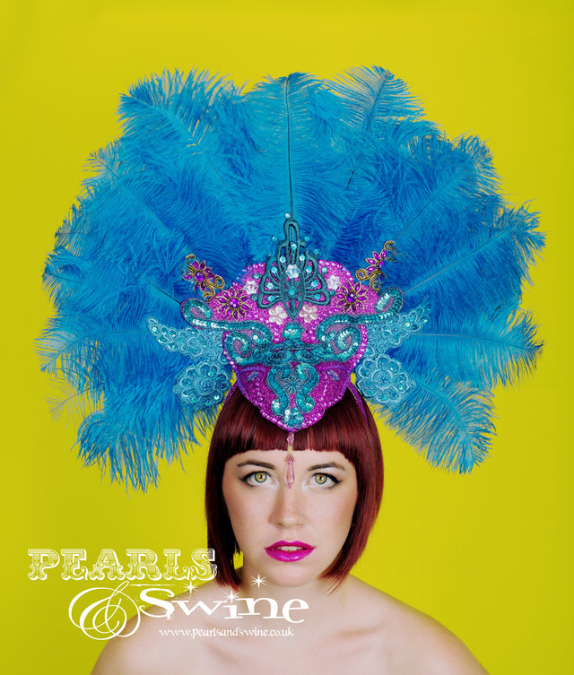 OTT carnival style, burlesque showgirl turquoise blue ostrich feather headdress set on a hand blocked felt base covered in fuchsia pink glitter and decorated with lace, sequin, gems and jewels. This is set on a wide headband, should you require any extra securing bobby pins will be fine.