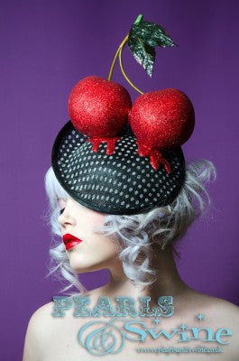 Huge cherries covered and dripping beautiful red glitter on a vintage style polka dot sinamay hat. This hat is set on a hidden base which attaches easily with a comb and adjustable hat elastic. Perfect headpiece for the races or a wedding.