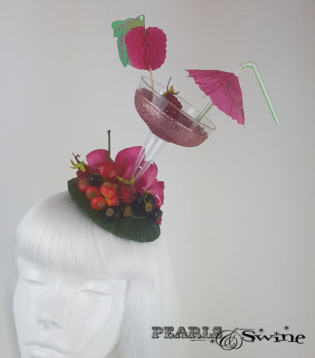 Pink glitter cocktail fascinator decorated with berries, cherries fruit, bougainvillea flowers and an umbrella